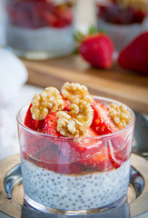 Chia pudding with strawberries walnuts and honey. Blurred background. White and red napkins 