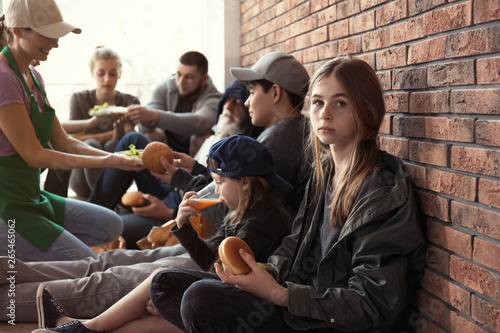 Cuadros en Lienzo Teenage girl with other poor people receiving food from volunteers indoors