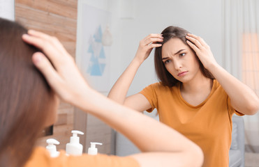 Young woman with hair loss problem looking in mirror indoors