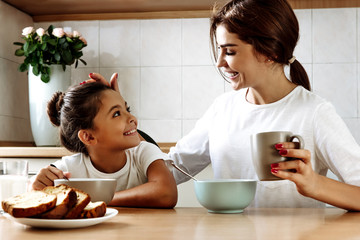 Family. Eating. Home. Mom and daughter are talking and smiling while having lunch in the kitchen at home