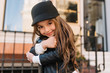 canvas print picture - Close-up portrait of amazing long-haired kid with wonderful kind smile posing outside, embracing iron pillar. Little stylish curly girl waiting for parents in front of building with fence