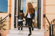 © Look! - Fashionable little girl wearing jeans and white sneakers comes out from clothe store holding mother's hand. Portrait of trendy woman in leather jacket after shopping with daughter in favorite shop.