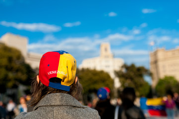 old woman wearing hat with venezuelan flag and country name in Barcelona city main square during march for regime change