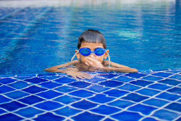 cute little boy feel happy play and swimming at swimming pool , sunny day and soft focus.