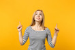 Portrait of excited joyful young woman in striped clothes pointing index fingers up isolated on yellow orange wall background in studio. People sincere emotions, lifestyle concept. Mock up copy space.