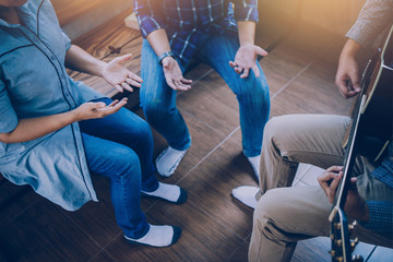 Group of  man and woman friends sitting on wooden chair while praise and worship God  by playing guitar and sing a song together in home office, Christian background small fellowship meeting concept.