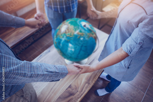 Three people standing and holding hands each other while pray to God for the world with blurred world globe on wooden table, Christian background for great commission or earth day concept.