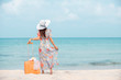 © Tawan - Relax  traveler woman in dress with sun hat holding suitcase standing on the beach  enjoys her tropical  vacation , lifestyle holiday travel  summer concept