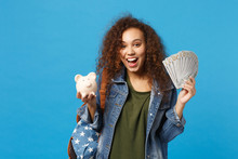 Young African American Girl Teen Student In Denim Clothes, Backpack Hold Pig Isolated On Blue Wall Background Studio Portrait. Education In High School University College Concept. Mock Up Copy Space.