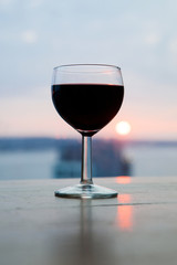 A glass of red wine in front of the beautiful soft sunset. Romantic dinner on the beach.