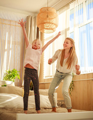 Wall Mural - Mother with child daughter having fun at home jumping on bed, happy parenthood