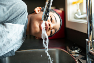 child afro american boy take water on his mouth and drink in a kitchen.