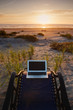 © Mint Images - Laptop on deck chair overlooking sunset on beach