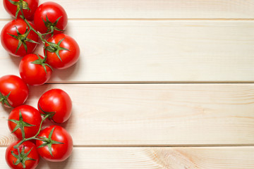 Red ripened tomatoes laid out at left side on light wooden background with copy space