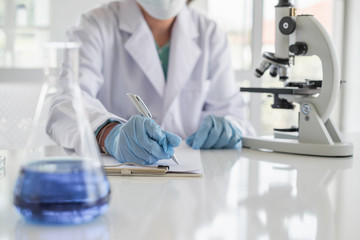 Wall Mural - a scientist hands writing on a clipboard in laboratory with test tube microscope and solutions.