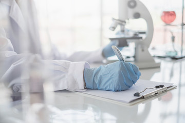 Wall Mural - a scientist hands writing on a clipboard in laboratory with test tube microscope and solutions.