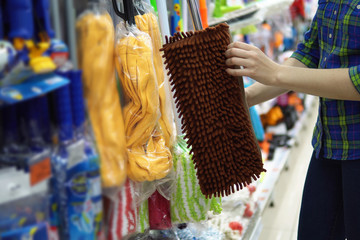 A young woman chooses a mop in the supermarket.