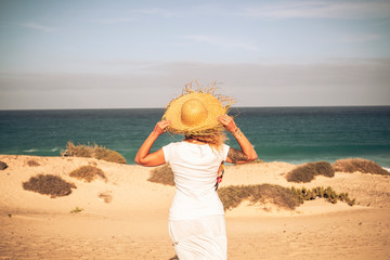 Summer holiday tourist vacation concept with people woman with white dress and hat viewed from back looking wonderful natural outdoor beach and feeling the breeze and the freedom