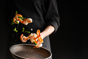 Seafood, Professional cook prepares shrimps with sprigg beans. Frost in the air, Cooking seafood, healthy vegetarian food and food on a dark background. Horizontal view. Eastern kitchen, banner