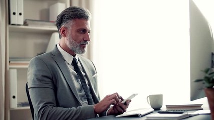 Wall Mural - A mature businessman with smartphone sitting at the table, working.