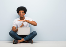Young Black Man Sitting On The Floor With A Laptop Doing A Timeout Gesture