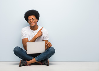 Young black man sitting on the floor with a laptop smiling and pointing to the side