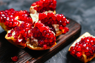 Pomegranate broken into pieces with red grains on a dark background.