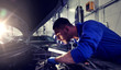 © Syda Productions - car service, repair, maintenance and people concept - auto mechanic man with lamp working at workshop