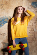 © Kiryl Lis - Portrait of positive young attractive girl wearing yellow blouse and blue jeans holding yellow skateboard.