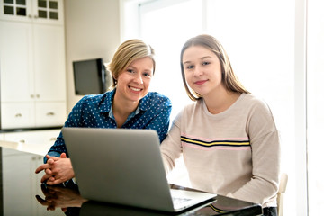 A mother using a laptop in kitchen with teenager