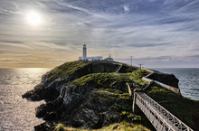The South Stack Lighthouse In North Wales With A Thrilling Sky And The Soon Setting Sun In The Background.