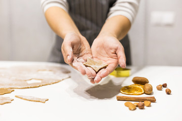 Wall Mural - Young pretty woman prepares the dough and bakes gingerbread and cookies in the kitchen. She holds a star cut from the dough in her hands. Merry Christmas and Happy New Year.