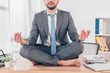 partial view of businessman meditating in Lotus Pose on office desk