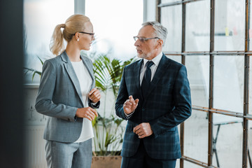 Wall Mural - attractive blonde businesswoman gesturing while talking with bearded businessman in eye glasses