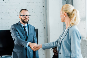 Wall Mural - handsome businessman in glasses shaking hands with blonde businesswoman