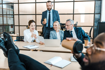 Wall Mural - selective focus of cheerful businessmen and businesswomen looking at digital tablet near african american coworker