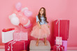 © Look! - Charming excited little girl in tulle skirt having fun, dancing on chair suround birthday presents, balloons isolated on pink background. Expressing true positive emotions, happiness of childhood
