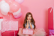 © Look! - Portrait cute birthday kid expressing to camera suround big giftboxes, balloons isolated on pink background. Amazing little girl with long brunette hair smiling with present on knees