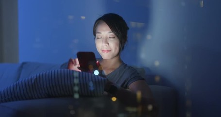 Poster - Asian woman look at the mobile phone at home in the evening with window reflection