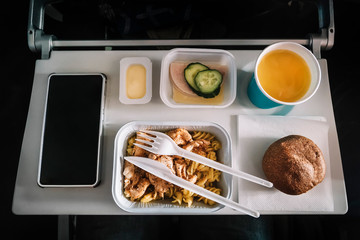 Inflight meal service tray for economy class, meat with pasta, seasoning fruit, salad, cucumber, a glass of juice and butter. selective focus