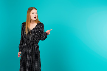 Wall Mural - Young woman pointing at copyspace isolated over turquoise blue background