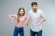 © Anastasia - Young guy and girl pointing down isolated over gray background