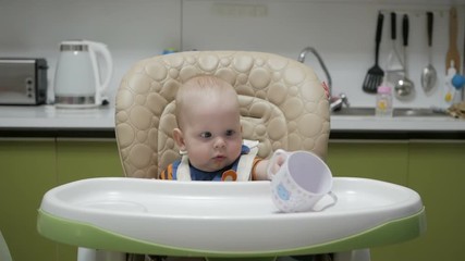 Baby sitting in a highchair and playing with a mug on a green kitchen