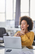 © nenadaksic - Serious mixed race businesswoman dressed casual sitting in modern office and using laptop.