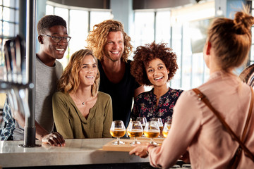 Wall Mural - Waitress Serving Group Of Friends Beer Tasting In Bar