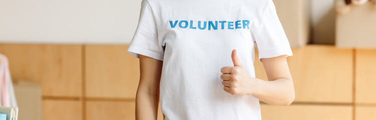 panoramic shot of volunteer in white t-shirt with blue volunteer inscription showing thumb up