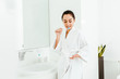 © LIGHTFIELD STUDIOS - brunette woman holding toothbrush with toothpaste and looking at hand