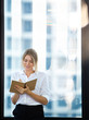 © NVB Stocker - Young business woman holding notebook and smile standing in front of office building windows