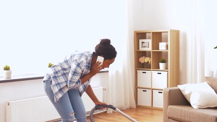 Wall Mural - people, housework and housekeeping concept - happy african american woman with vacuum cleaner calling on smartphone at home