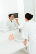 © LIGHTFIELD STUDIOS - selective focus of happy young woman brushing teeth and looking at mirror in bathroom